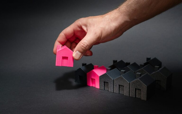Mano colocando una casa entre una hilera de viviendas